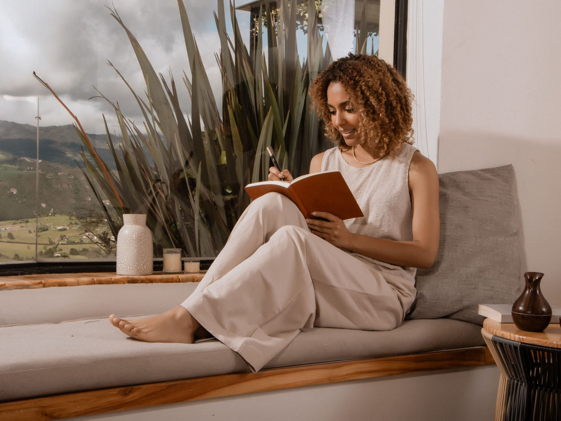 Relaxed solopreneur journaling by the window, practicing mindful planning to balance work and well-being.
