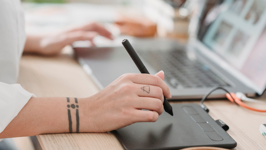 Close-up of a solopreneur using a digital drawing tablet while working on a laptop, creating faceless digital content.